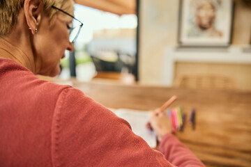 A photo from the back, of a senior woman using crayons and coloring the coloring book.