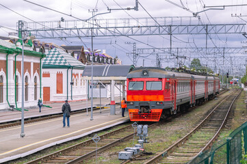 Fototapeta premium Electric transport on the railway. Contact power lines for commuter trains. People get on an electric train on the platform. Railway tracks at the railway station.Transportation of passengers by train