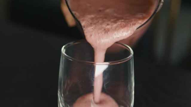 Pouring thick pink berry fruit smoothie from blender into glass. Close up.