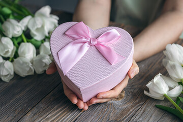 Gift box in the shape of a heart in a female hands on a wooden background.