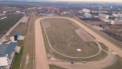 Aerial flyover footage of a racetrack  in Ploiesti Romania. Modern hippodrome track for horse and chariot racing. Racecourse seen from the air on a cold winter afternoon. Dirt oval track flyover.
