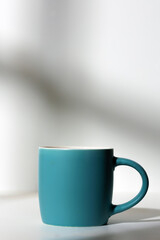 A cup of coffee stands on a white background with a shadow from the window in the morning light