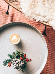 A Scandinavian Christmas setting with coffee, holly and pine foilage and a fluffy skin covered chair