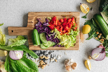 Sliced cabbage, bell pepper and cucumber on a wooden kitchen board, top view.