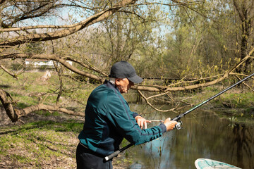 Mature man attaching tackle on rod during fishing.
Fisher in casual clothes attaching tackle on rod while standing on riverbank and catching fish from river