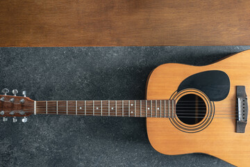 Acoustic guitar on a textured black and wooden background, top view.