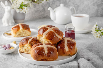 Traditional Easter hot cross buns on a white plate with butter, berry jam and cup of tea. Delicious Easter breakfast.