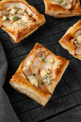 Mini tarts with puff pastry, pieces of pear, blue cheese, walnuts and honey on a concrete background. Top view.