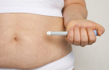 Woman hand holding self injection pen near her stomach. Medicine and treatment concept