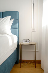 Blue king size bed with crisp white bedding and digital alarm clock on the nightstand under beautiful morning sunlights