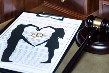 A clipboard holding a prenuptial agreement with a cut-out silhouette of a couple and wedding rings,...