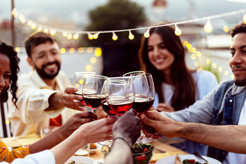 Happy people celebrating summer party toasting with red wine gathered at home terrace.