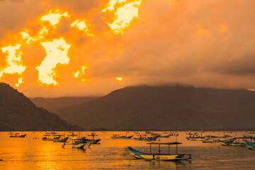 Tranquil scene of colorful boats floating on a bay at sunset, with mountains silhouetted in the background.