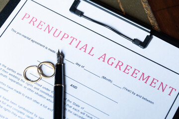 Close-up of a prenuptial agreement form with wedding rings and a fountain pen, indicating the legal...