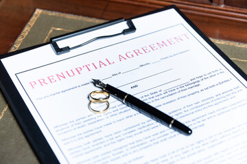 Close-up of a prenuptial agreement form with wedding rings and a fountain pen, indicating the legal aspects of marriage preparation.
