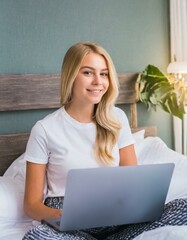  smiling attractive young woman sitting in bed in front of her laptop
