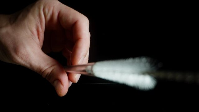 Close-up of a man's hand cleaning a glass tube with a brush, moving it back and forth inside.