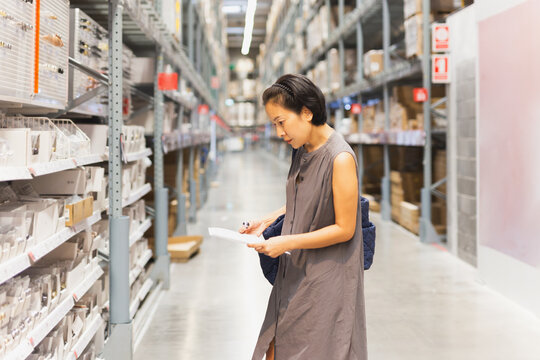 Woman holding paper choosing household goods in warehouse.