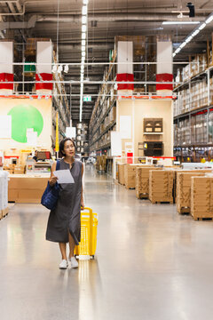 Woman with cart looking for houshold goods on a warehouse.