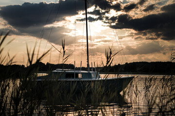 A beautiful sunset over a lake somewhere in Poland. The boat moored at the pier in the reeds gently rocks on the small waves. Romantic evening by the water. Sailing is a great passion