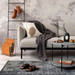 Exquisite and modern composition of living room interior with design grey sofa, chair, round pedant lamp, black coffee table, decoration, pillow and elegant accessories. Concrete grunge wall.