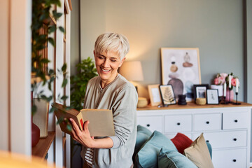 A smiling senior adult woman with short hair enjoying a book in her apartment