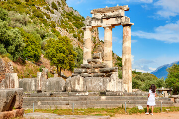 A long hair woman in a white dress looking at the ancient temple complex of Athena Pronaia in...