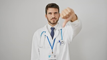 Angry young hispanic guy in white coat, showing thumbs down sign. bad vibes and negative expression from this unhappy doctor with stethoscope, isolated on white wall. total dislike!
