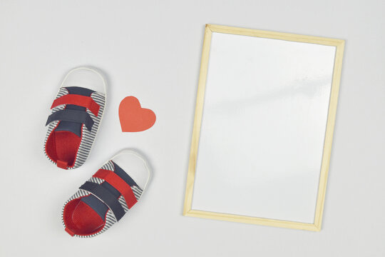Baby shoes with paper heart and empty whiteboard on the side. accessorize new baby concept.