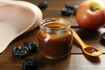Tasty baby food in jar, spoon and dried prunes on wooden table, closeup