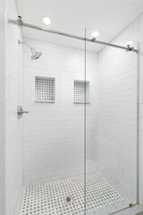 A walk-in shower with white subway tiles, sliding glass door, chrome showerhead, and two niche...