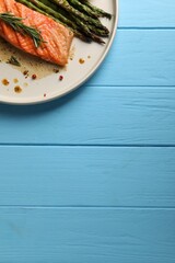 Tasty grilled salmon with asparagus and spices on light blue wooden table, top view. Space for text