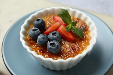 Delicious creme brulee with berries and mint in bowl on table, closeup