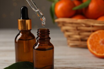 Tangerine essential oil dripping from pipette into bottle on wooden table, closeup