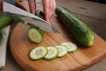 Woman cutting cucumber on wooden board at table, closeup