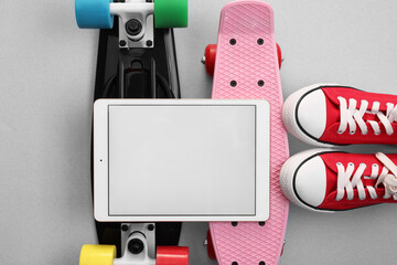Modern tablet, skateboards and shoes on light grey background, flat lay. Space for text © New Africa