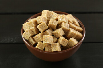 Brown sugar cubes in bowl on black wooden table, closeup
