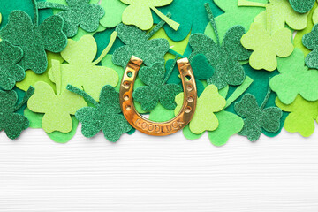 St. Patrick's day. Golden horseshoe and green decorative clover leaves on white wooden table, flat lay