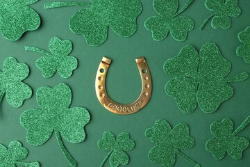 St. Patrick's day. Golden horseshoe and decorative clover leaves on green background, flat lay