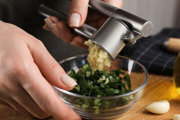 Woman squeezing garlic with press at wooden table, closeup