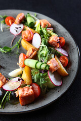 Healthy salad for lunch. Red fish salad with radish and fresh cucumber. Micro-greens and cherry tomatoes on a plate. A lean dish. Healthy food. Dark background. Vertical photo.
