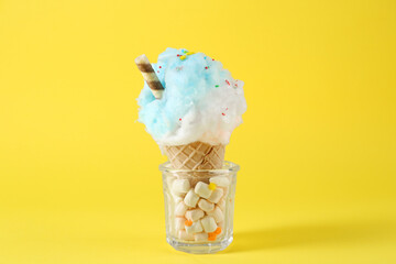 Sweet cotton candy in waffle cone on yellow background