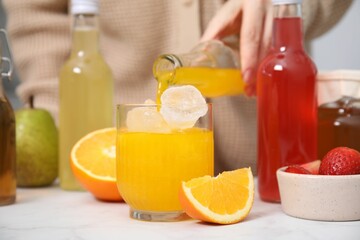 Woman pouring tasty kombucha into glass with ice at white table, closeup