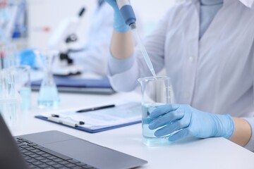 Fototapeta premium Scientist dripping sample into beaker in laboratory, closeup