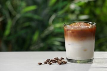 Glass of iced coffee and beans on white wooden table outdoors. Space for text