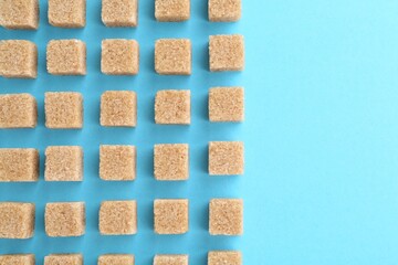 Brown sugar cubes on light blue background, top view. Space for text