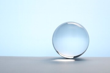 Transparent glass ball on table against light blue background. Space for text