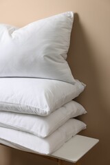 Fototapeta na wymiar Stack of soft white pillows on table near beige wall
