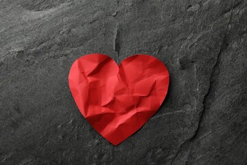 Fototapeta premium Crumpled red paper heart on dark grey table, top view. Broken heart
