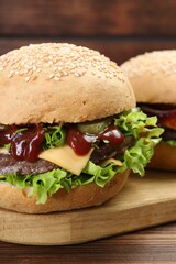Board with delicious cheeseburgers on wooden table, closeup